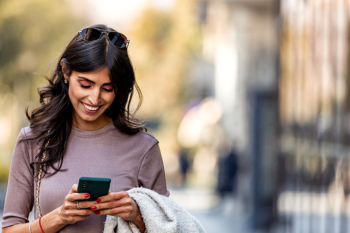 Woman on sidewalk looking at cell phone and smiling