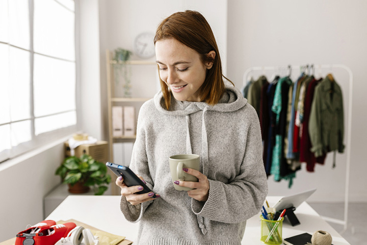 Woman at home holding mug and cell phone