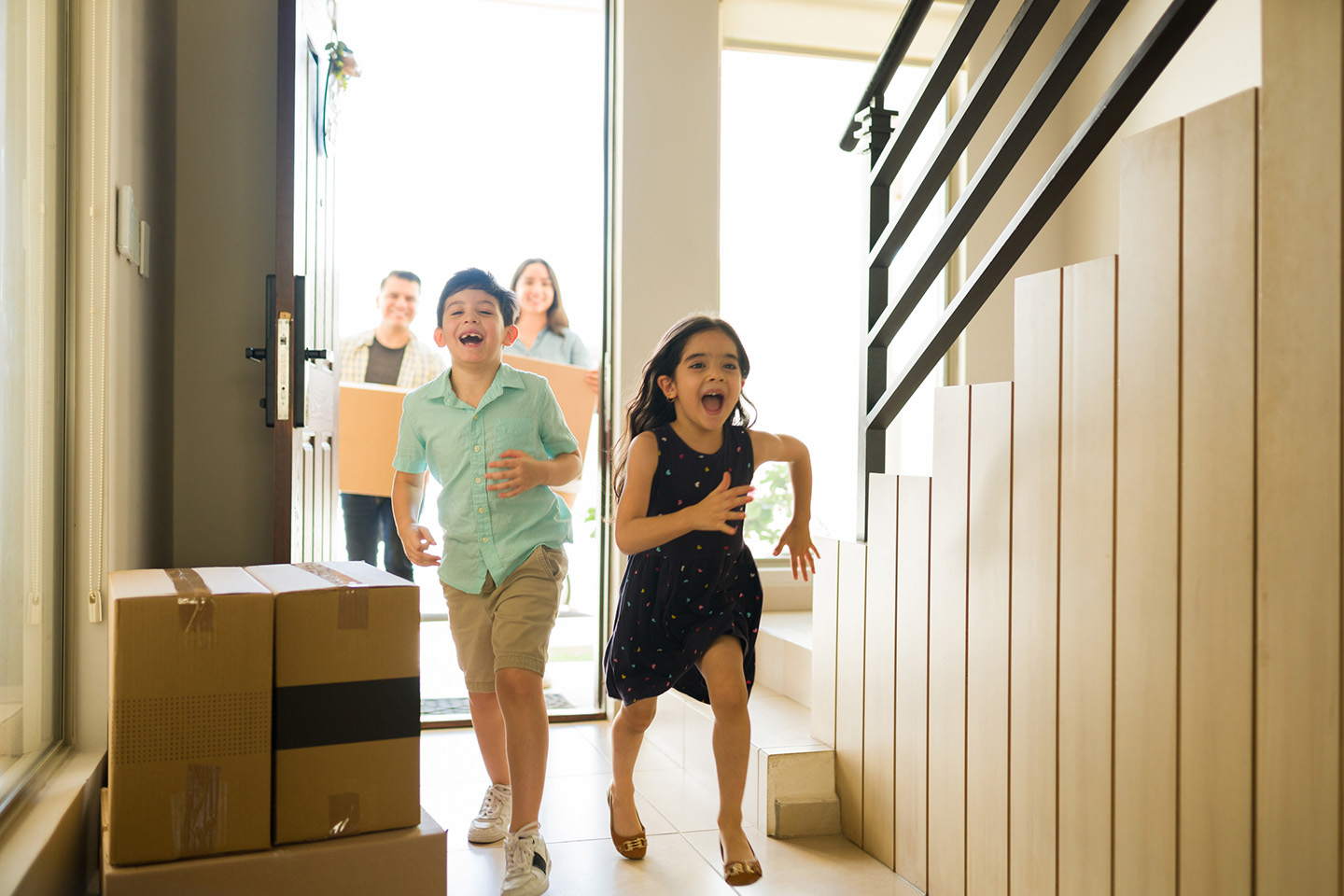 FHA_1440 Parents and two kids run into their new home carrying moving boxes